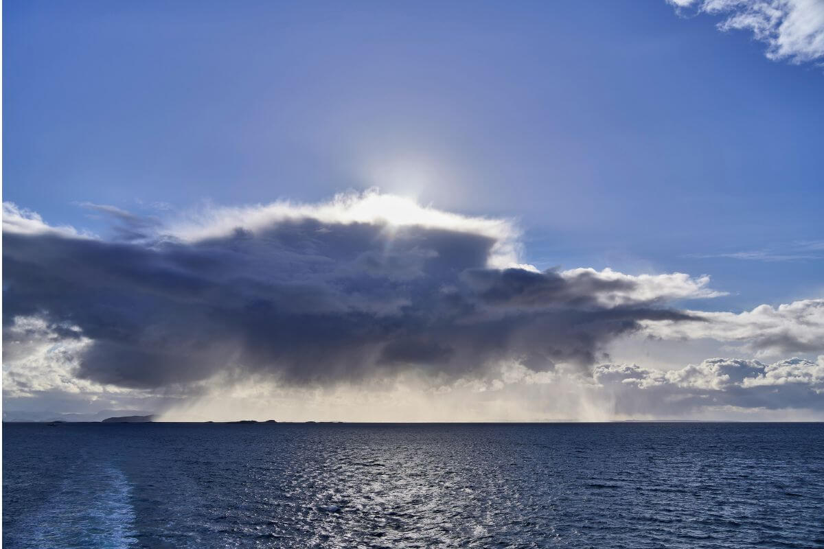 Dark storm cloud over the ocean with sunlight breaking through above the water.