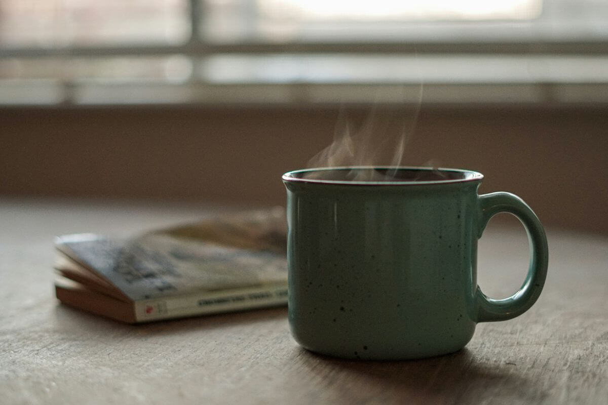 Steaming mug on a wooden table beside books in soft morning light, symbolizing calm and stress awareness.